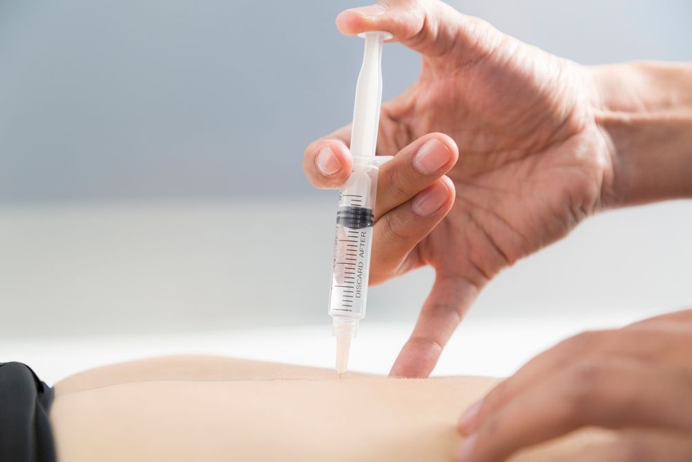 Hand using a syringe to inject a beige material into a mold or tray