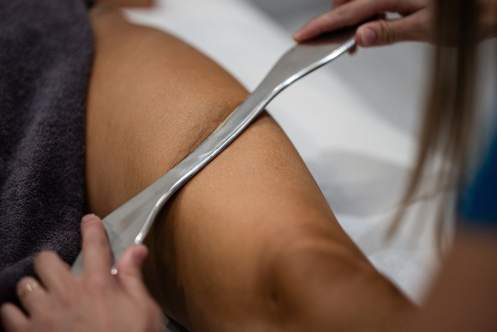Therapist using a metal scraping tool on a patient’s shoulder during a treatment session