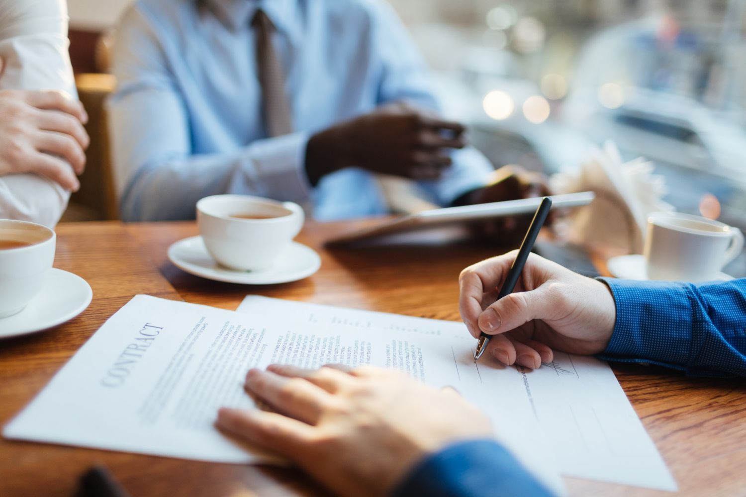 People signing a document at a meeting table with coffee cups in a bright office setting
