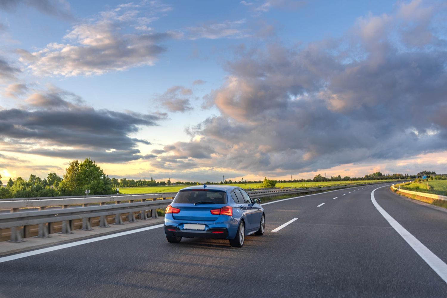 Blue car driving on a highway at sunset under cloudy skies