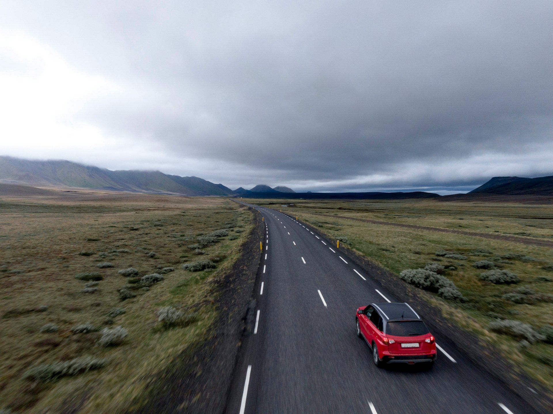 Red pickup driving on an empty rural road under a cloudy sky.