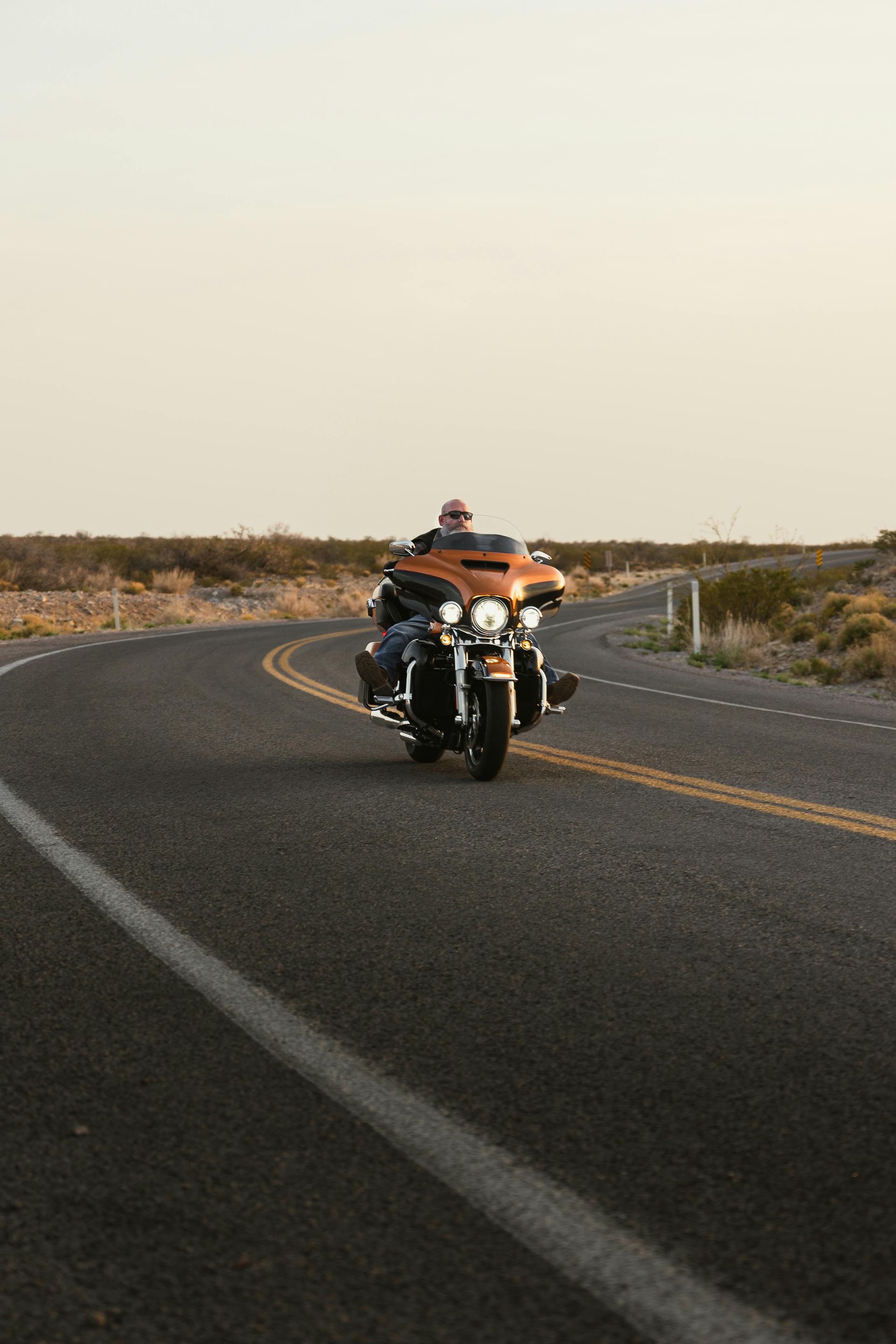 Motorcyclist riding on a winding desert road at sunset