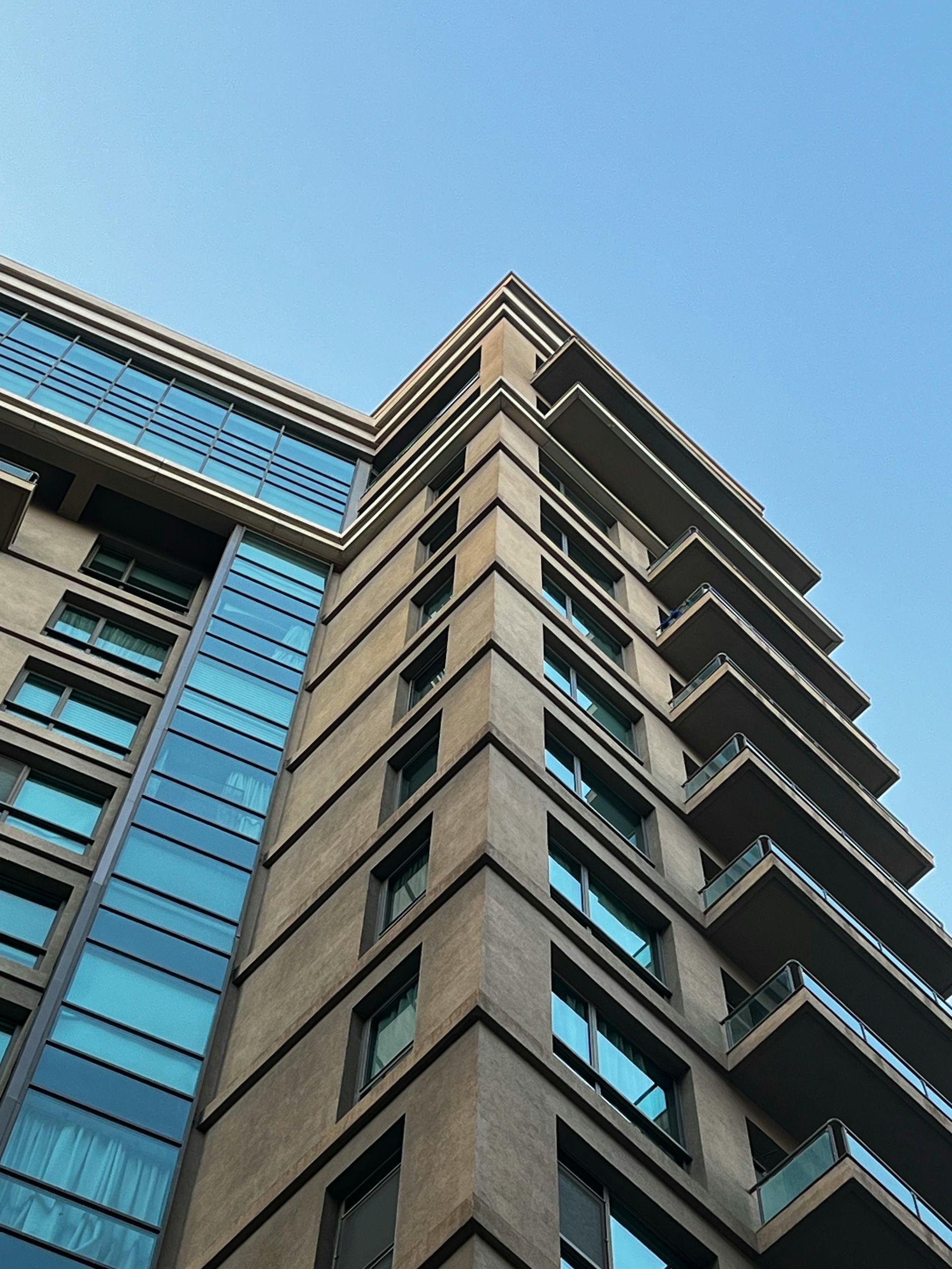 Low-angle view of a modern high-rise building with gray concrete and blue glass windows against the sky