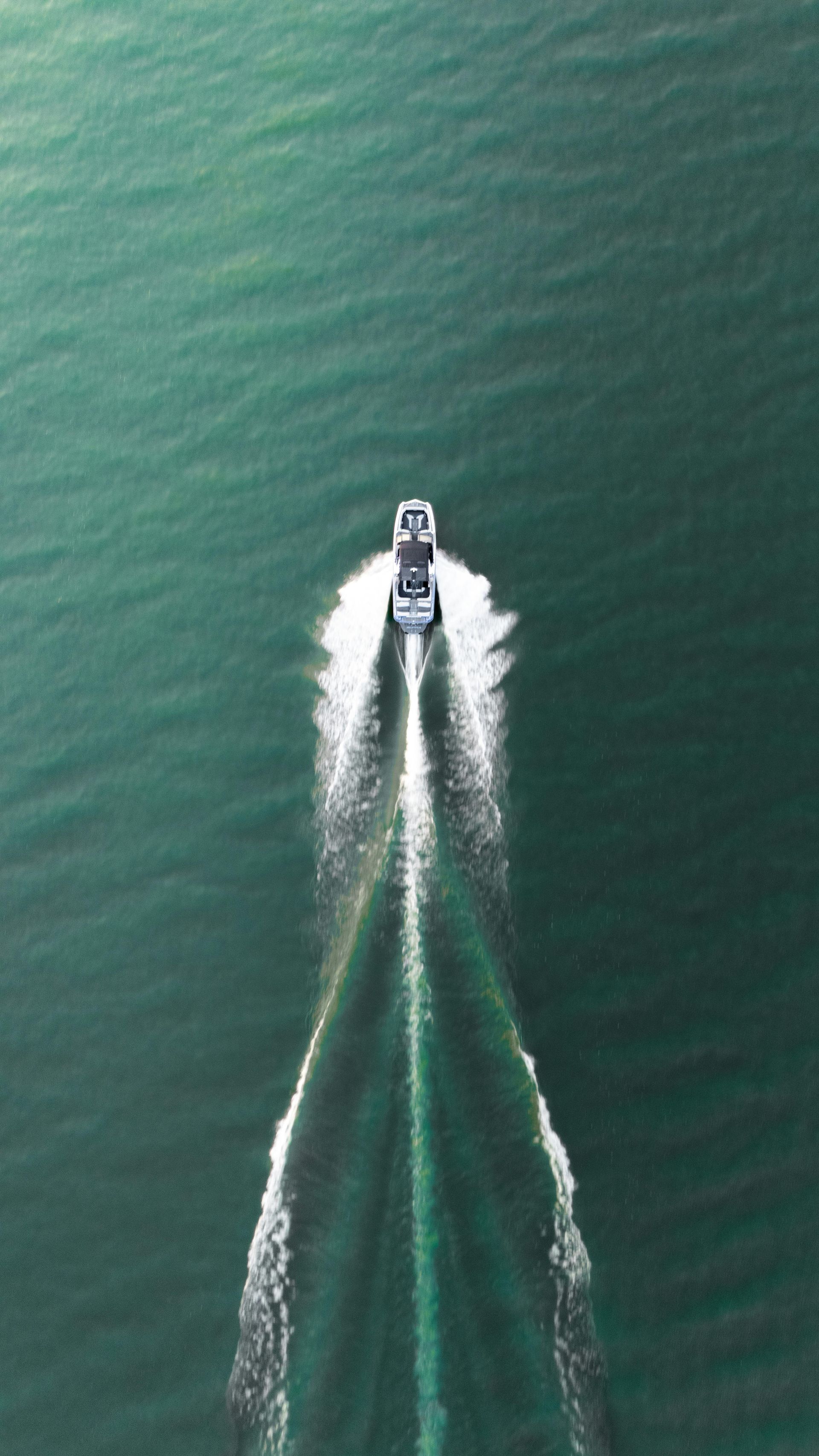 Speedboat leaving white wake on green water, viewed from above.