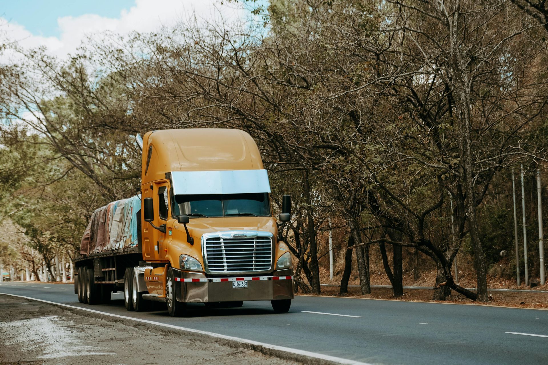 Orange semi-truck driving on a tree-lined road in a wooded area