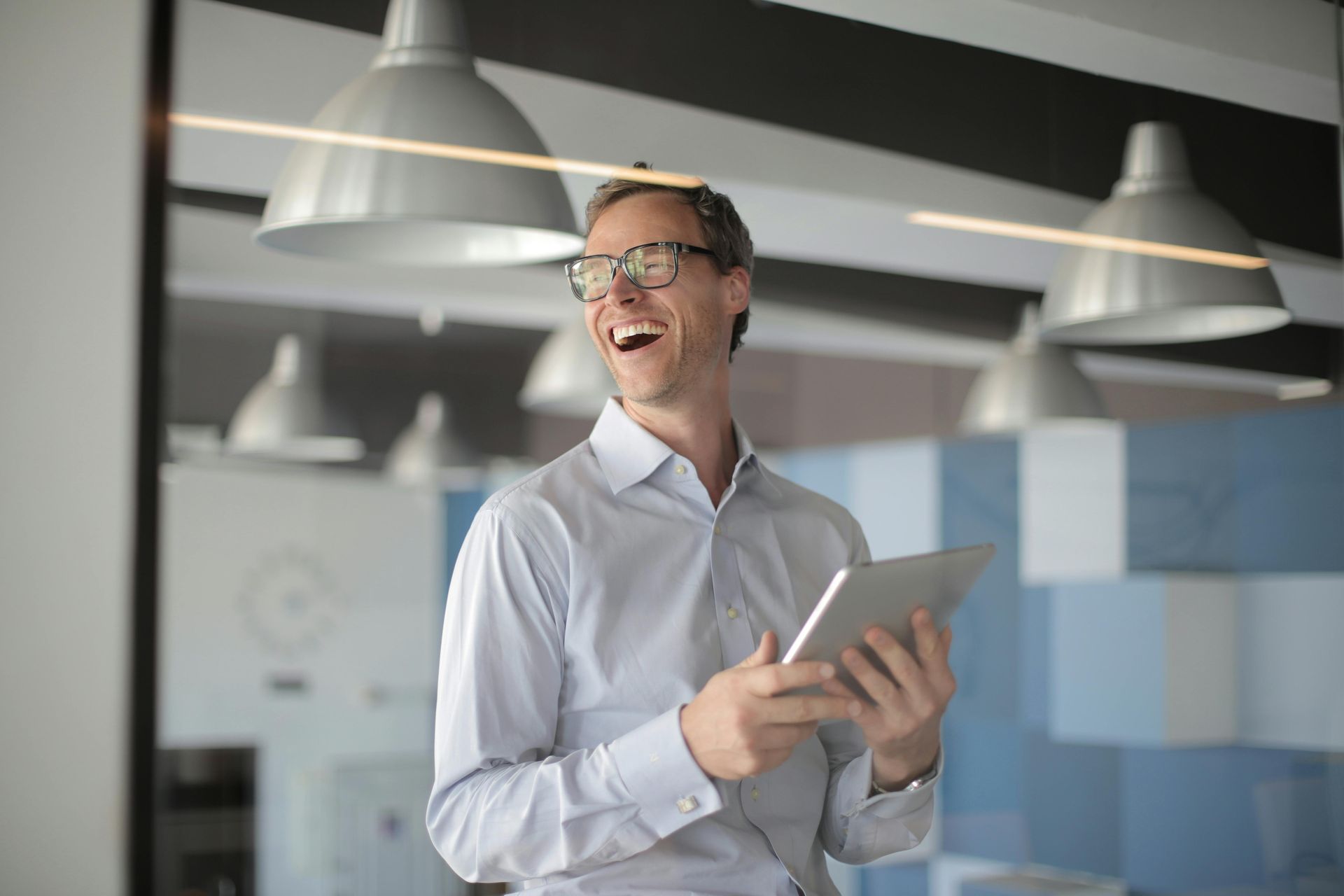 Smiling person holding a tablet in a modern office with hanging lights