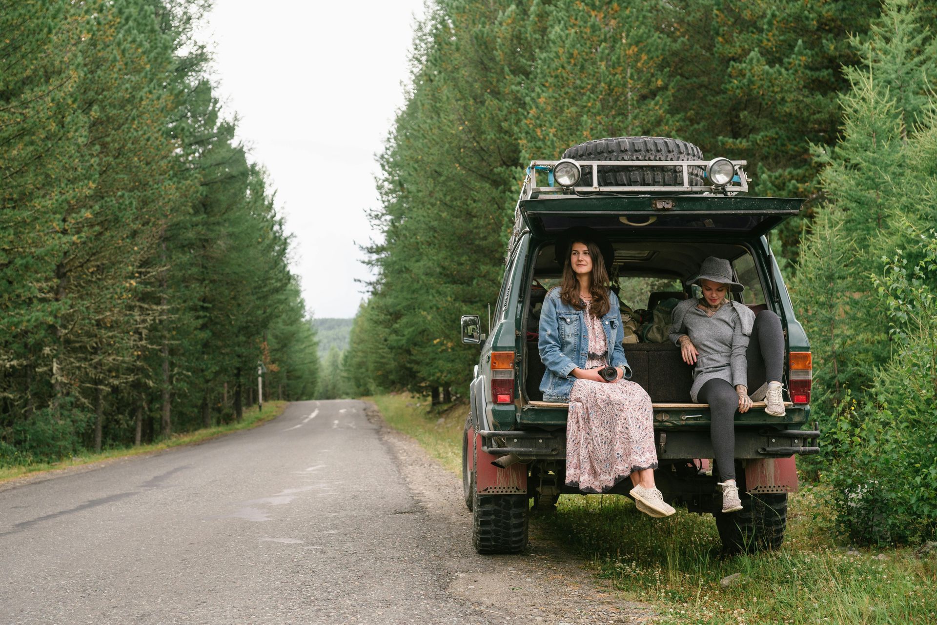 Two people sitting on the back of a green off-road vehicle on a forest road