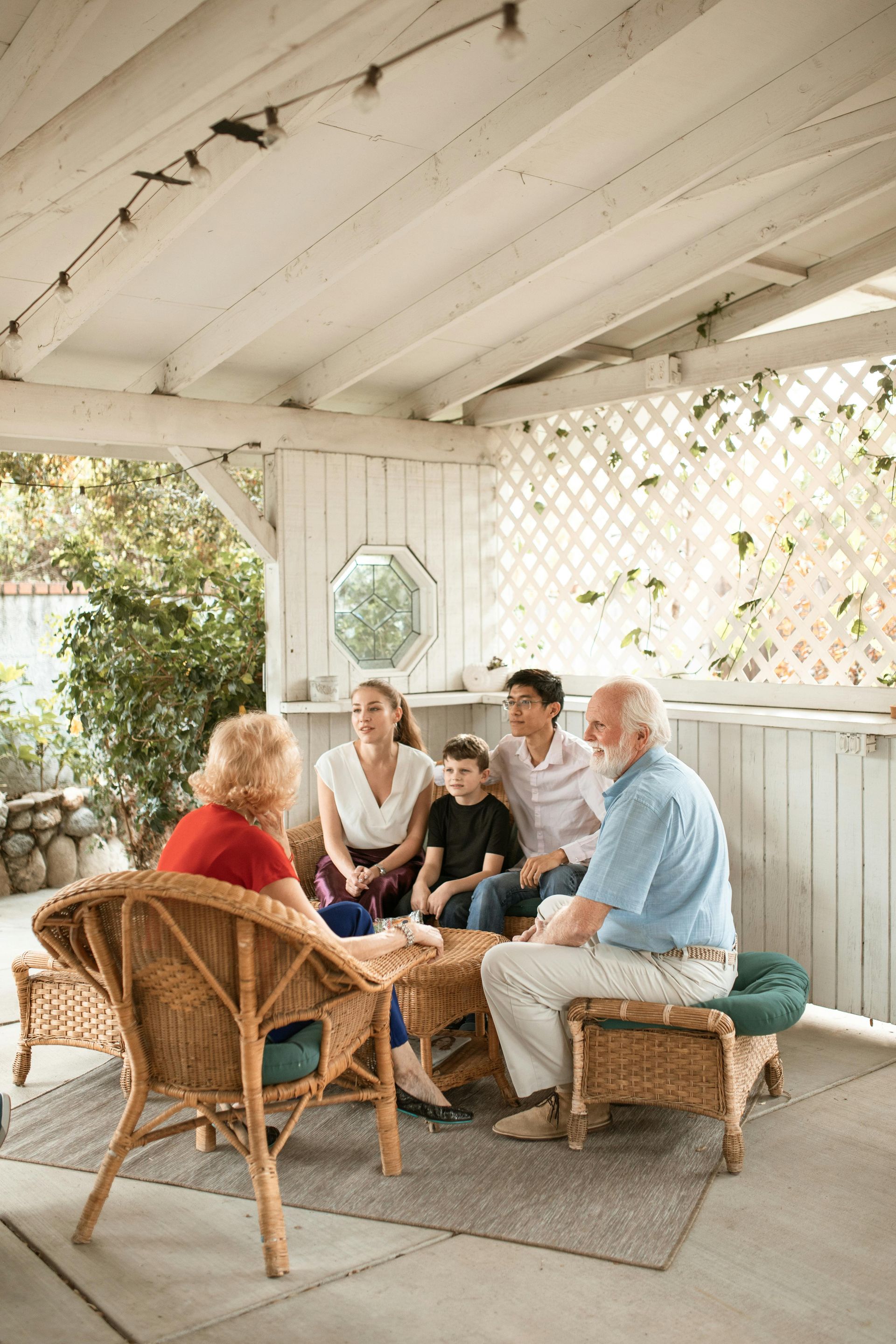 People sitting together on a covered porch in wicker chairs, chatting around a low table.