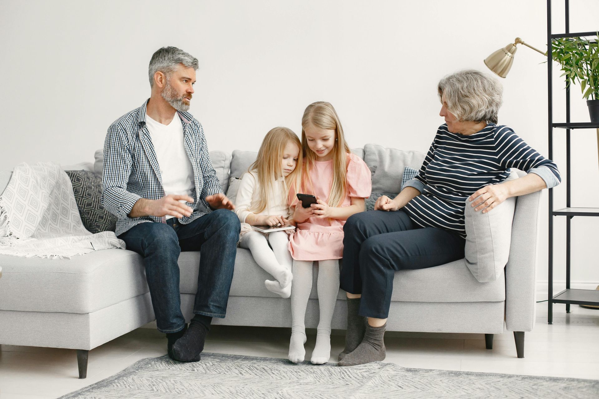 Family sitting on a couch, children focused on a tablet while adults talk beside them
