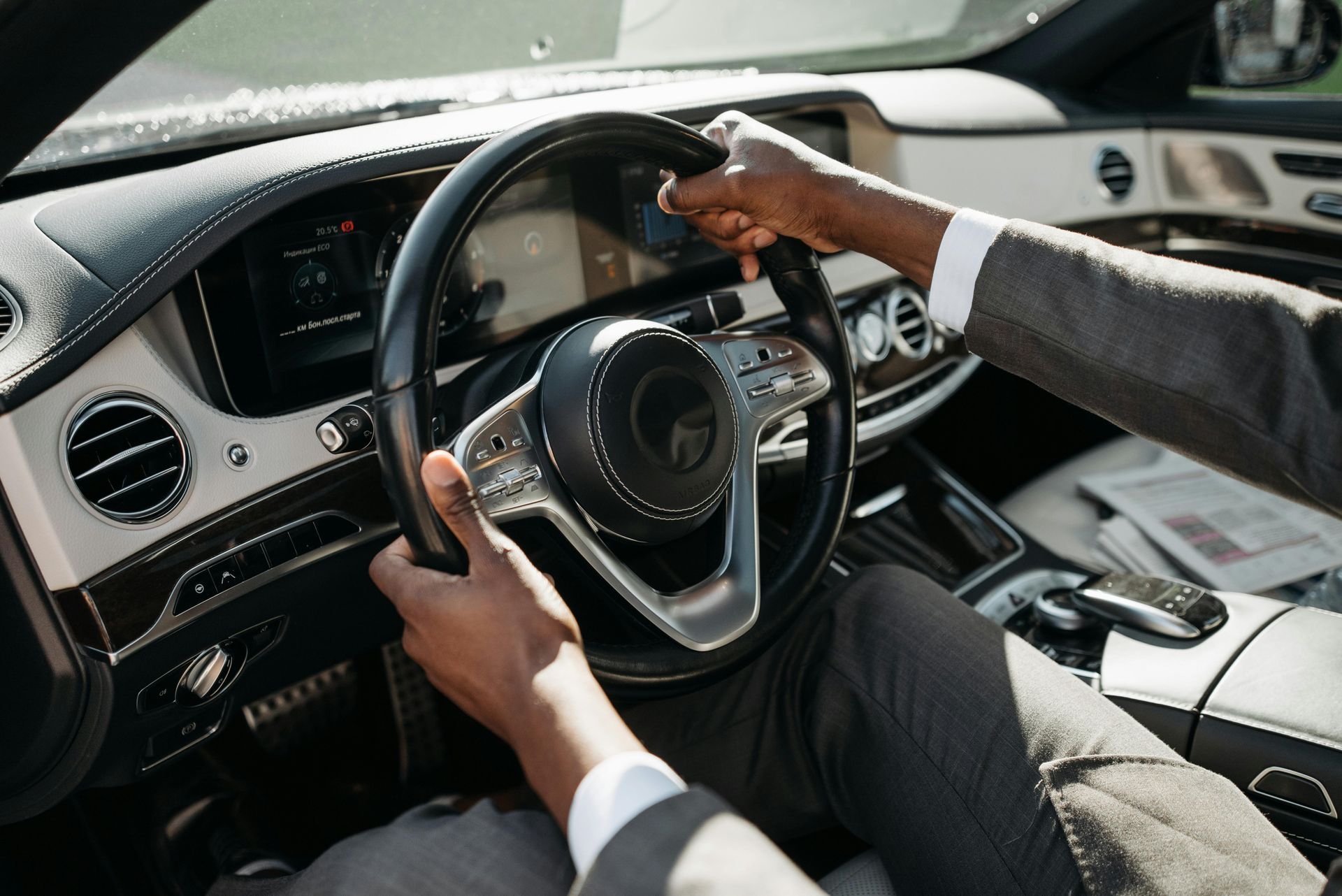 Driver holding steering wheel inside a luxury car interior, dashboard and center console visible
