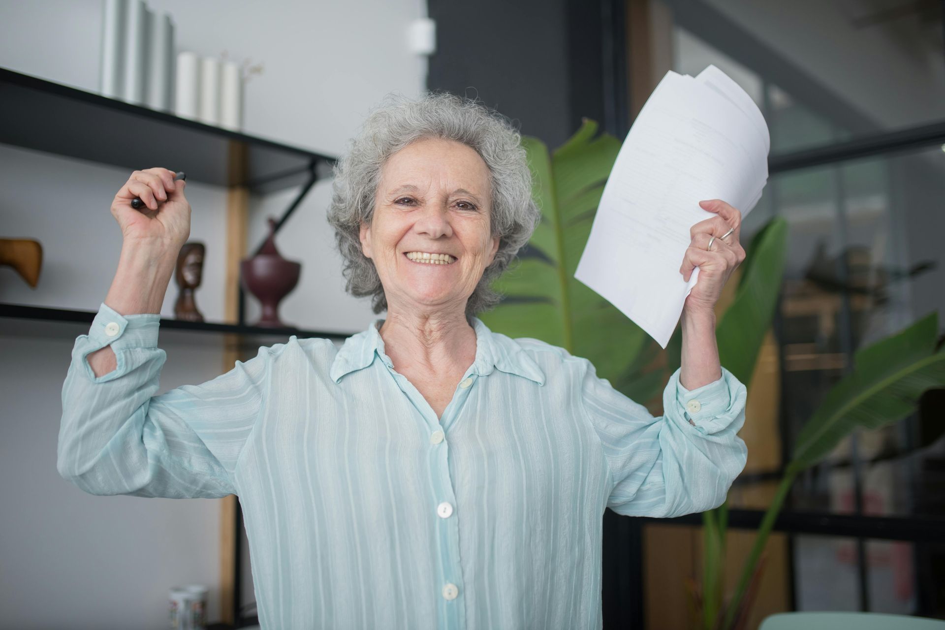 Smiling person in a light blue shirt holding up a sheet of paper indoors