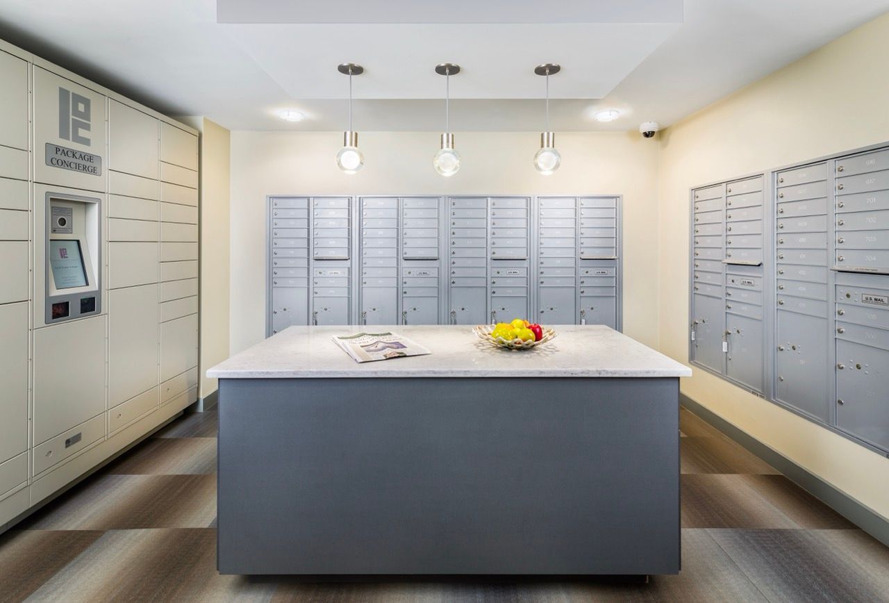 Interior of a modern apartment mailroom with rows of gray mailboxes and a central island.