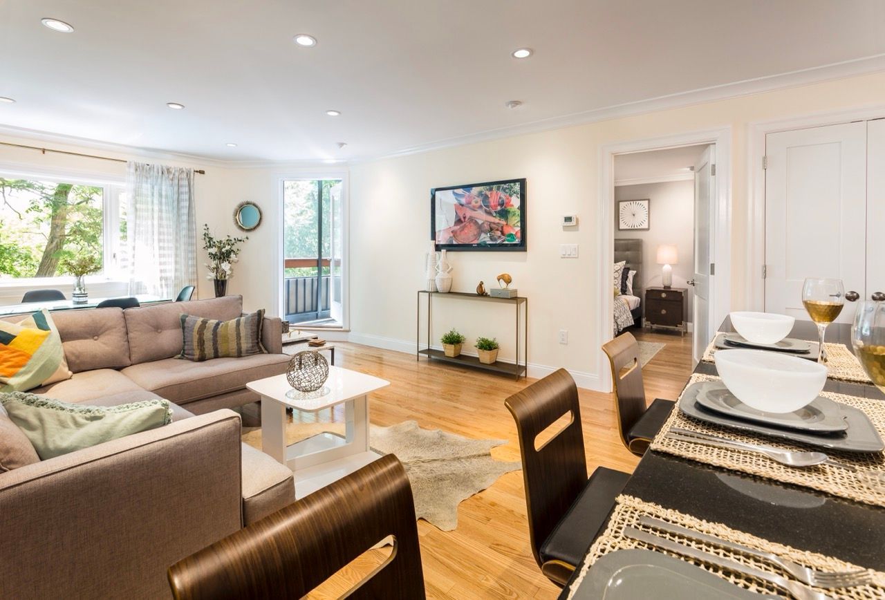 Open-concept living room with beige sectional, glass coffee table, TV, and dining area by balcony door.