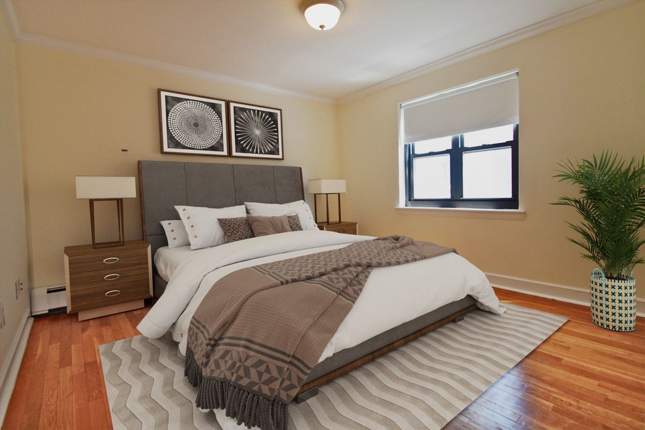 Bedroom in an apartment with a queen bed, nightstands, lamps, plant, and window.