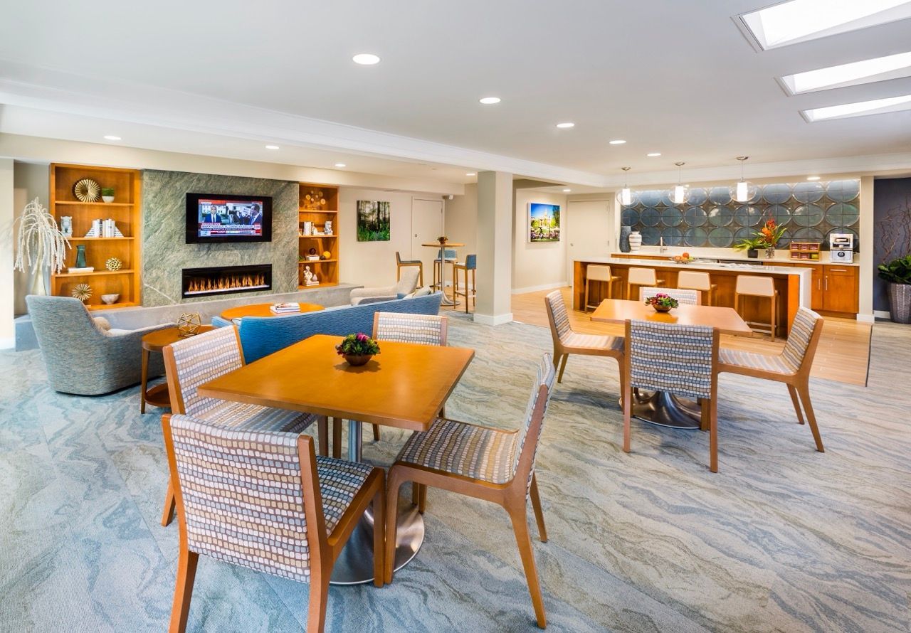 Spacious modern community lounge with seating, a fireplace, and a bar/kitchen area.