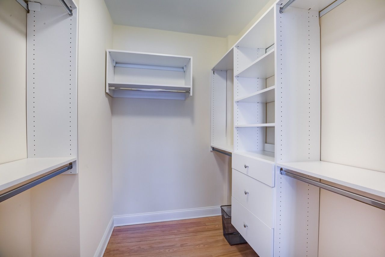 Bright walk-in closet with white built-in shelves, drawers, and hanging rods.