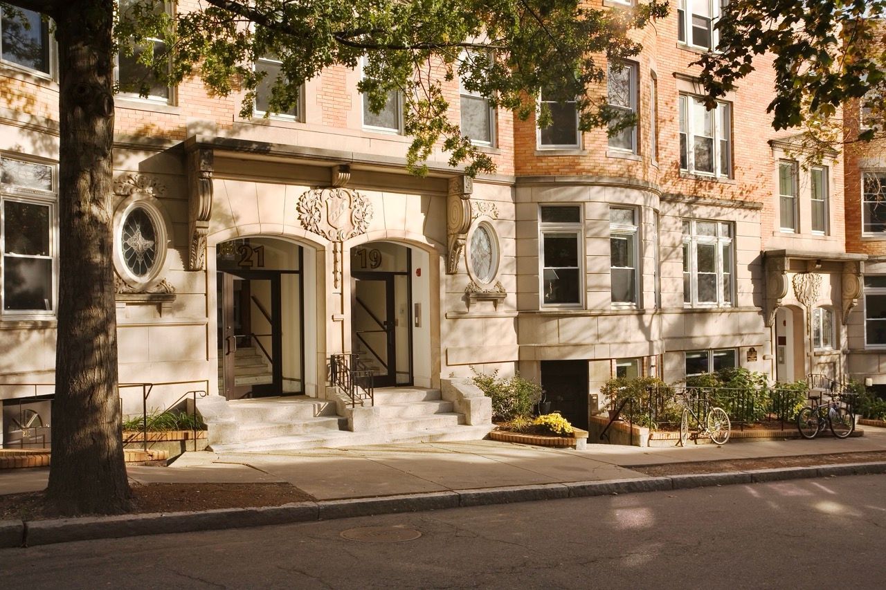 Brick apartment building exterior with ornate arched entrance, steps, and parked bicycles.
