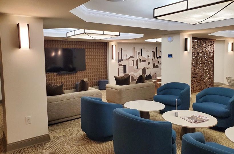 Indoor resident lounge with blue curved chairs, round white tables, and wall art.
