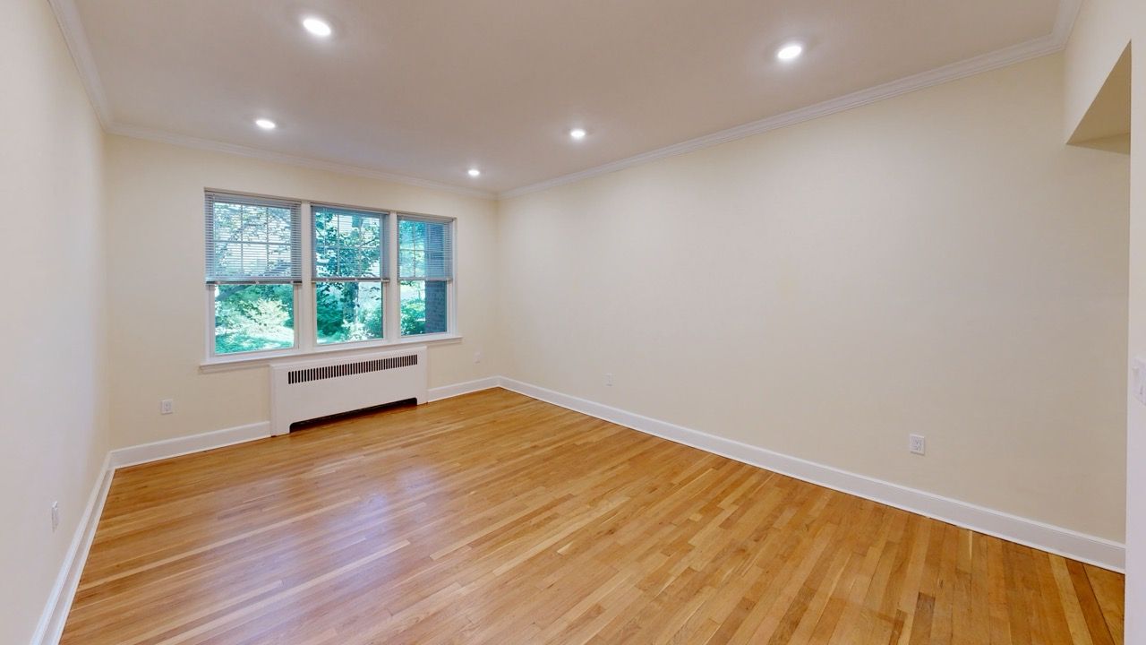 Empty living room with hardwood floors, beige walls, and large windows.