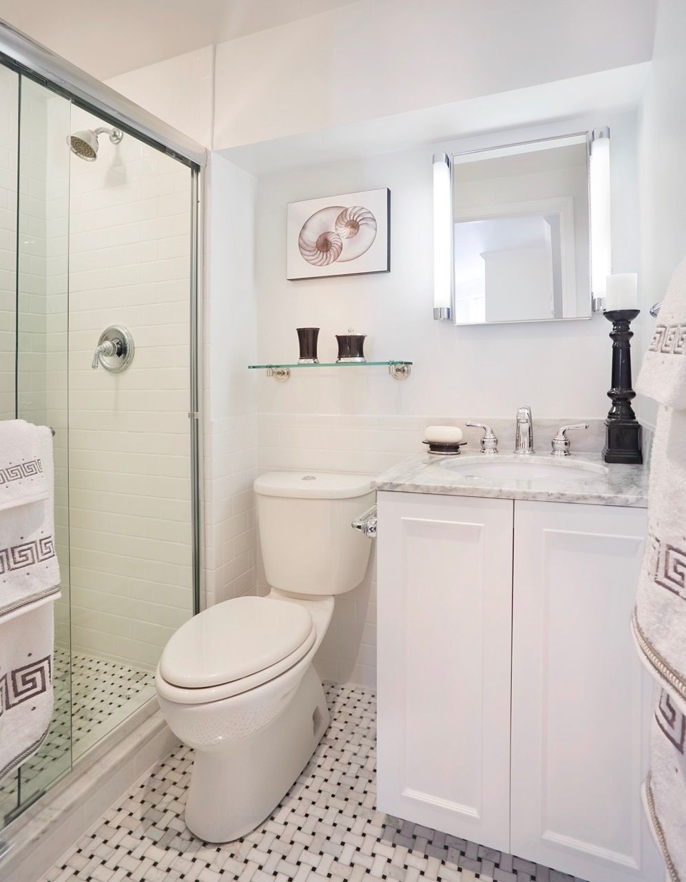 White modern bathroom with a glass shower, toilet, and marble-topped vanity.