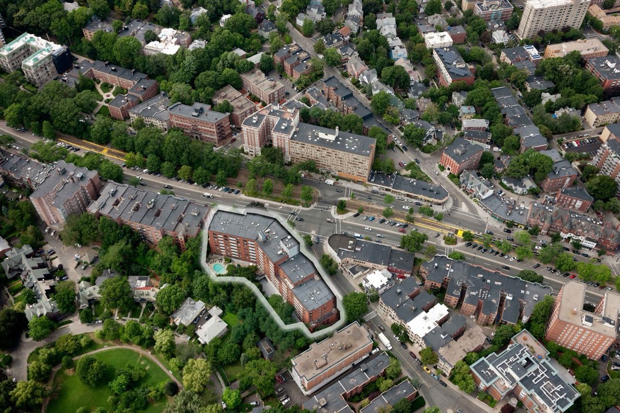 An aerial view shows a dense urban neighborhood with red-brick buildings, green trees, and winding streets.