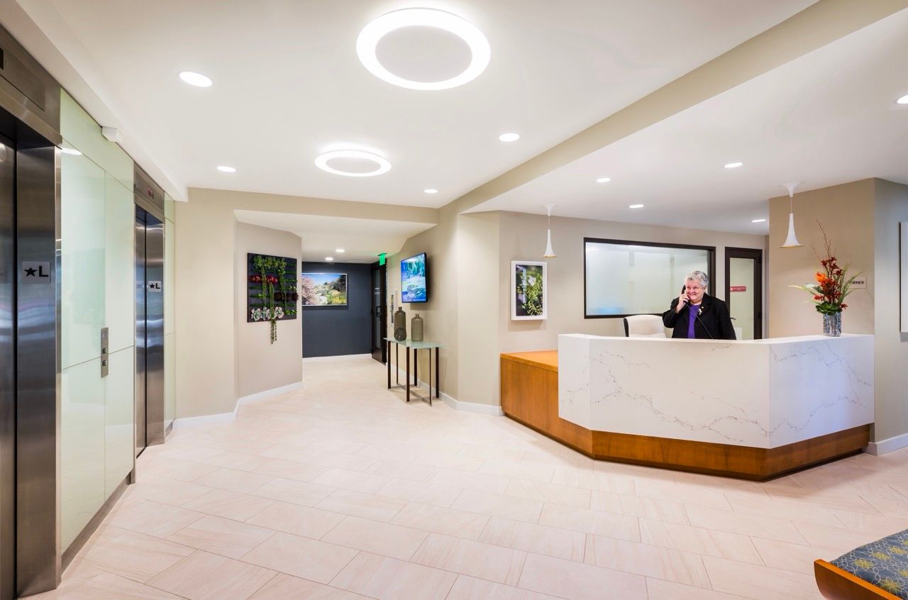 Lobby reception area with a curved marble desk, elevators, and a receptionist.