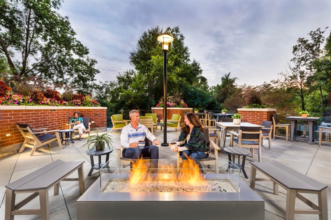 Outdoor rooftop lounge with a fire pit, surrounding seating, and greenery.
