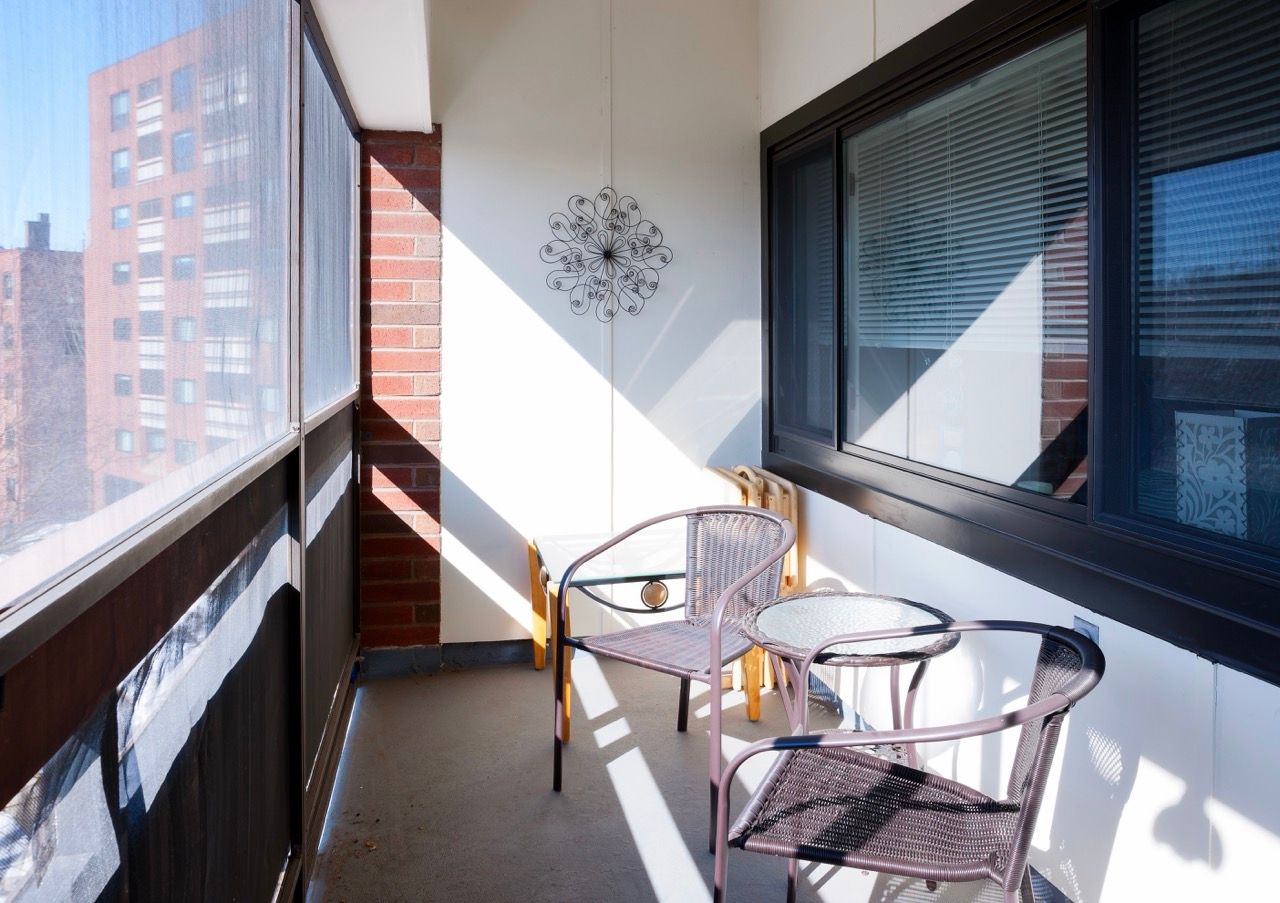 Balcony with metal chairs and a glass table outside an apartment, sunlit.