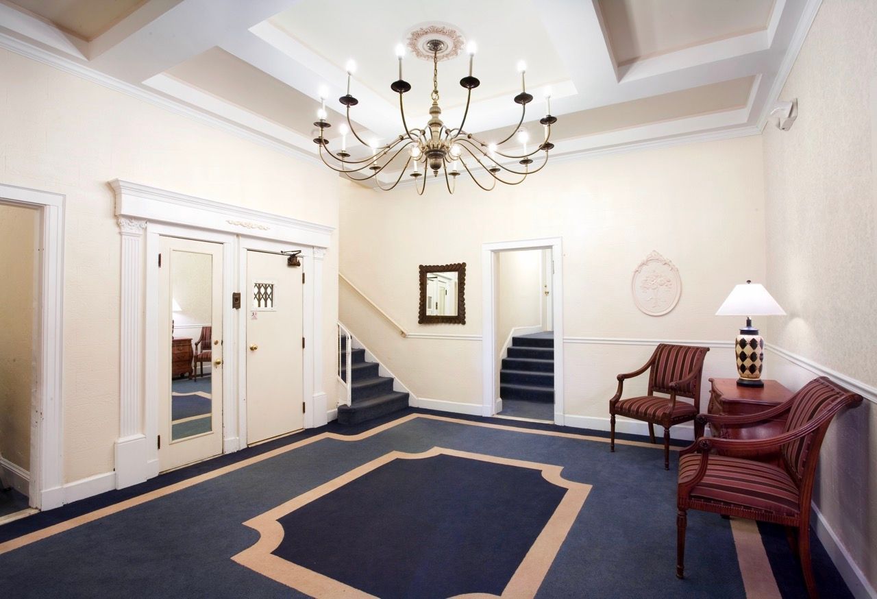 Interior building lobby with chandelier, stairs, doors, and seating.