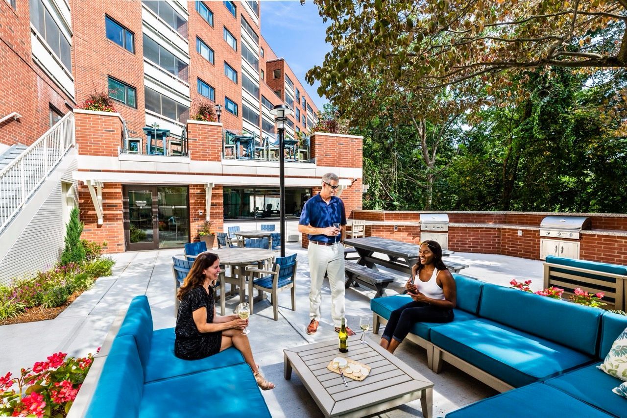 Outdoor communal terrace with blue seating, tables, and people socializing near a brick apartment building.