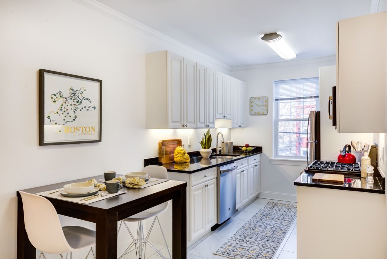 Bright white kitchen with white cabinets, black countertops, stainless appliances, and a small dining table with place settings.