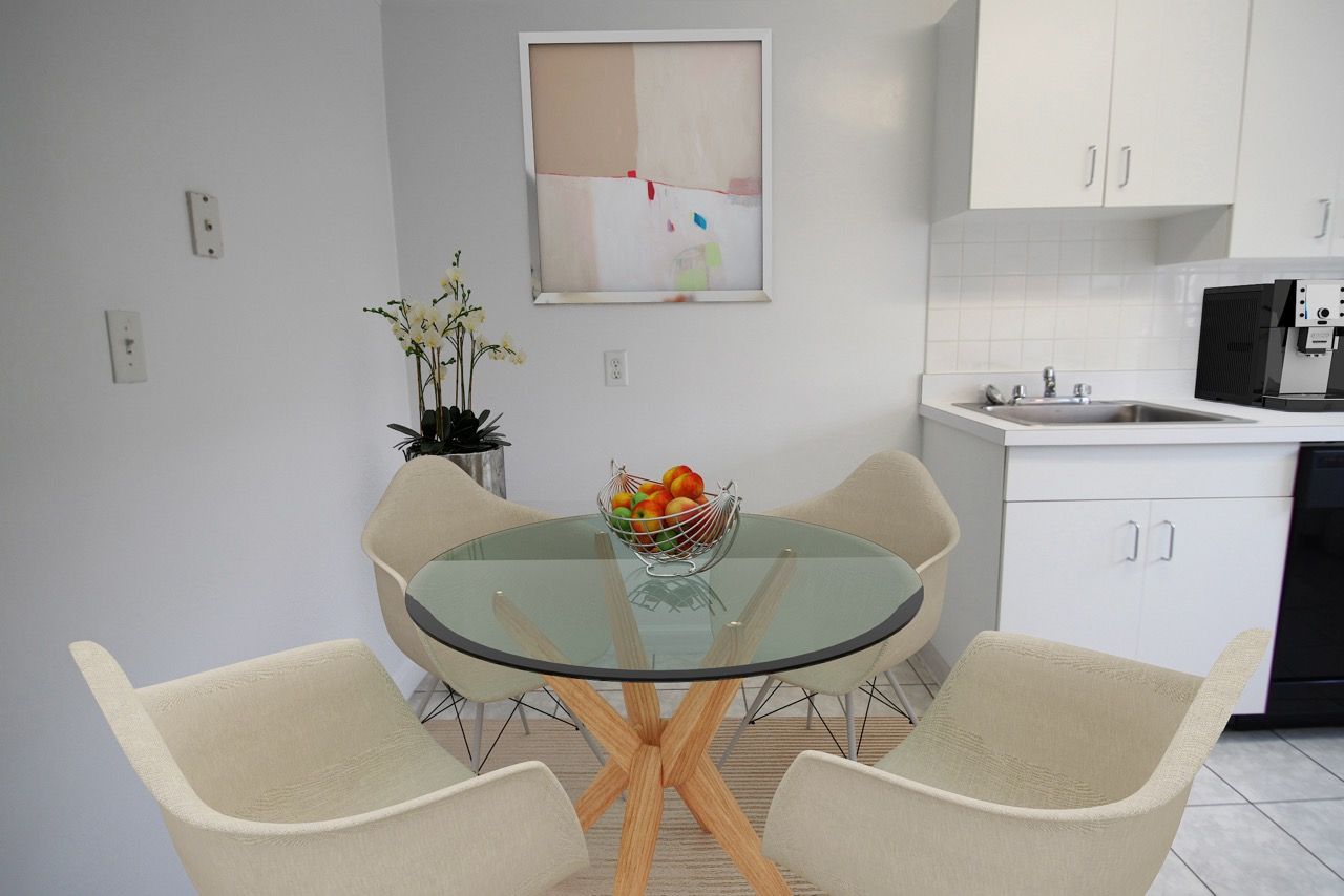 Dining nook with round glass table and beige chairs in a small apartment kitchen.