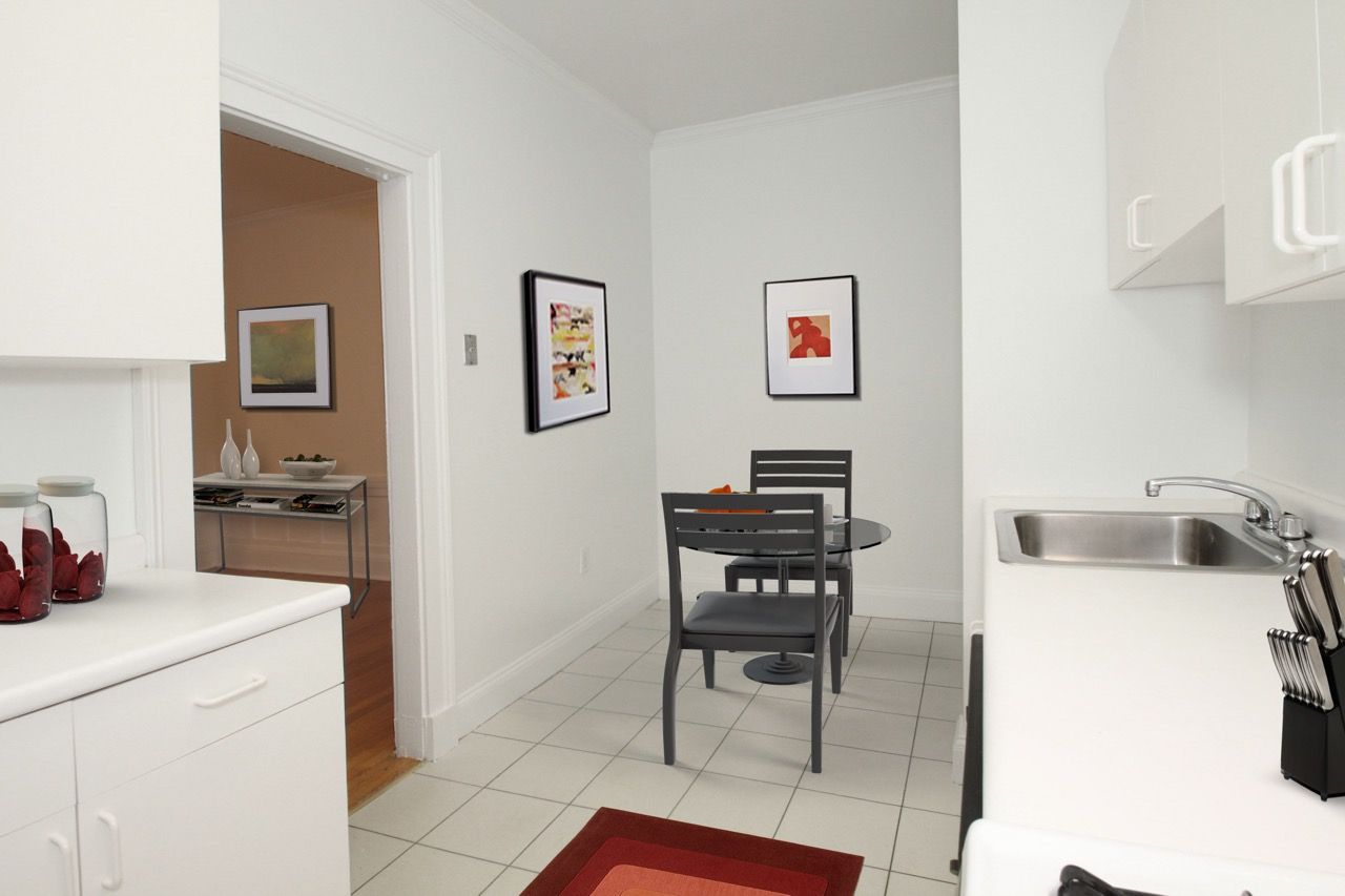 Interior view of a compact apartment kitchen and dining area with a round glass table and gray chairs.