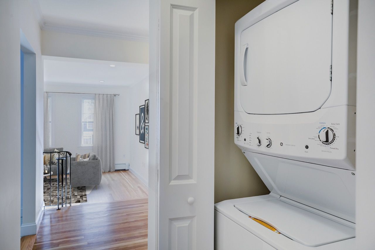 In-unit stacked washer and dryer inside a closet near the hallway with a living room visible