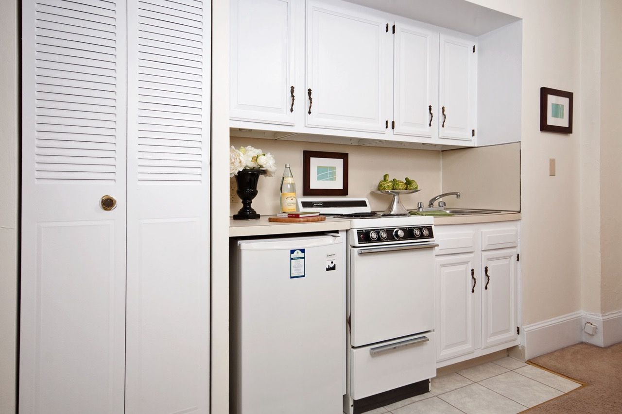 White kitchen with upper cabinets, a stove, sink, and small refrigerator.