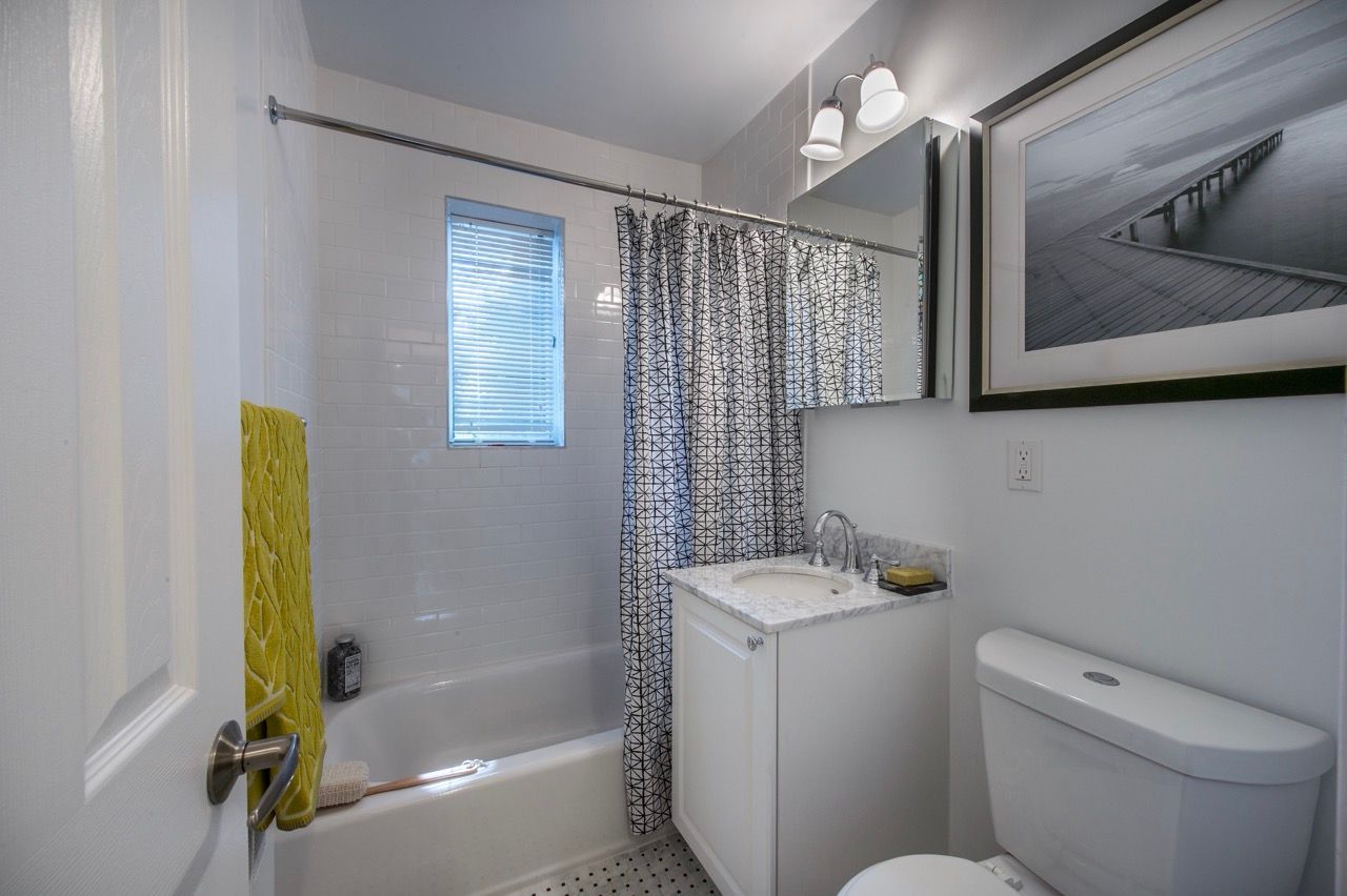 Small apartment bathroom with tub/shower, white vanity, and toilet.