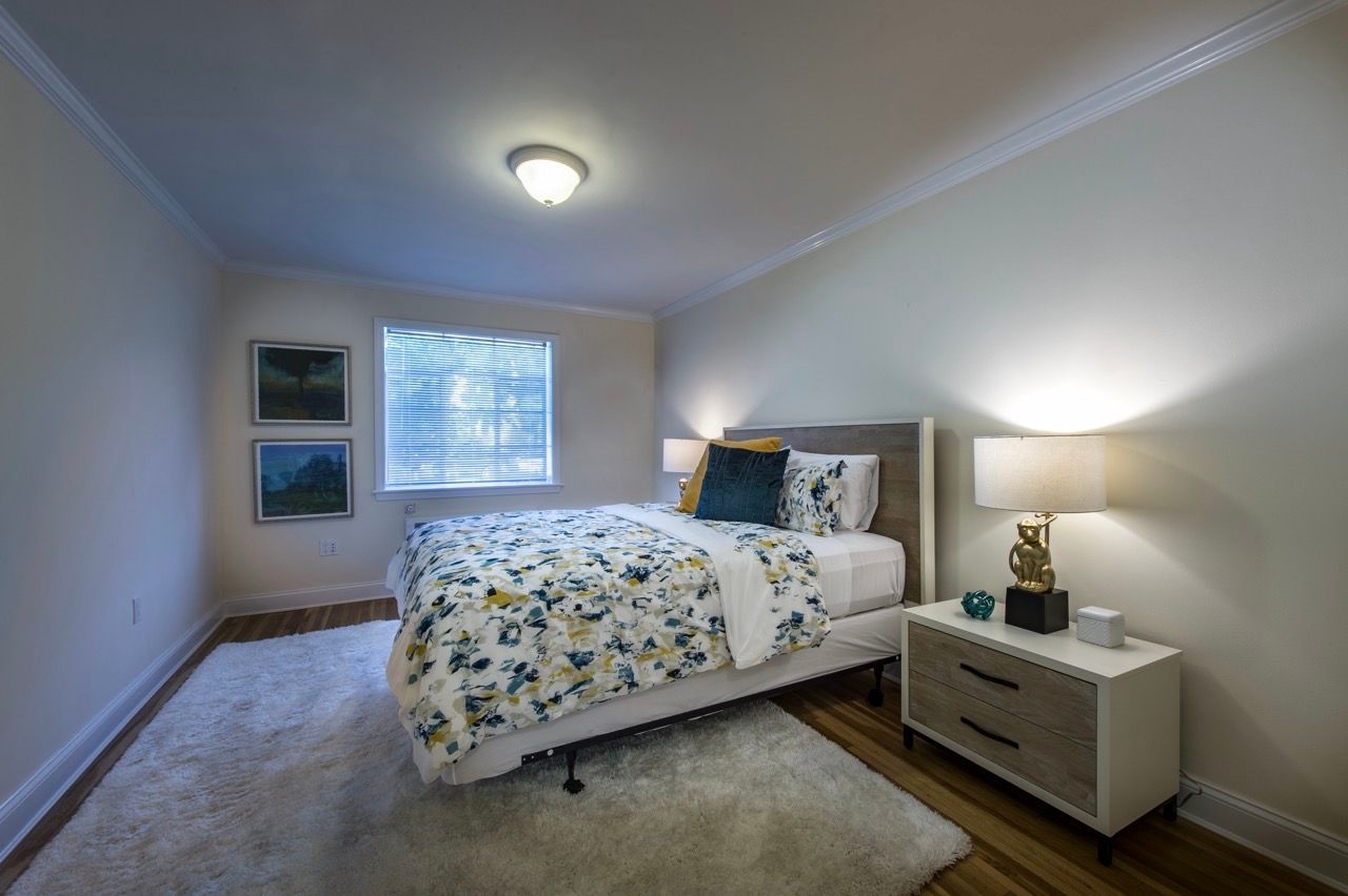 Cozy apartment bedroom with a queen bed, two nightstands, lamps, window, and a plush rug.