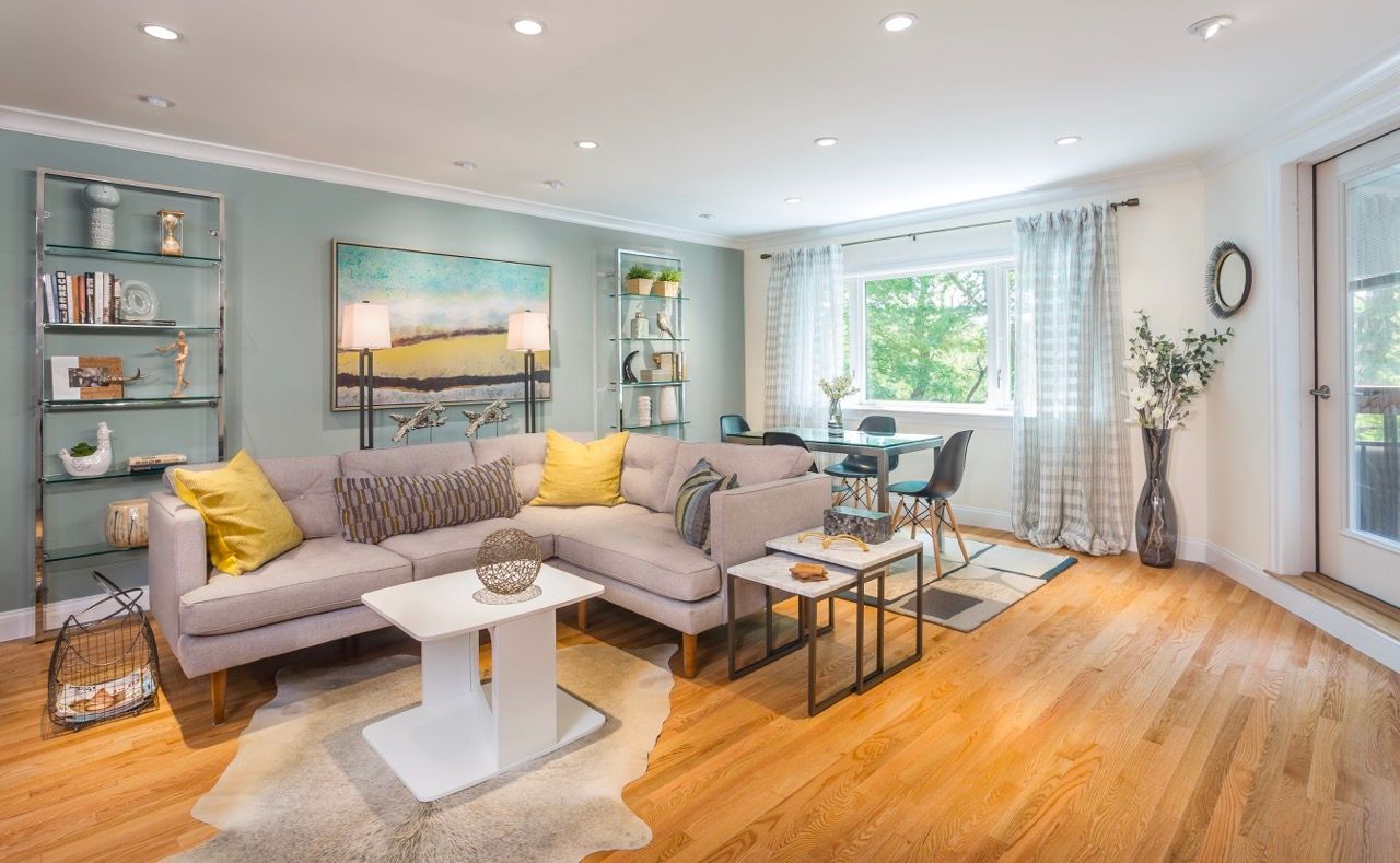 Bright, open-concept living room with a beige sectional, wood floors, and a dining area by a large window.