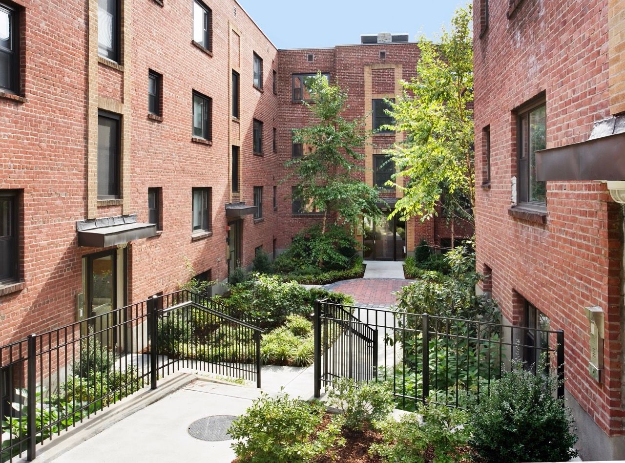 Brick apartment courtyard with trees, shrubs, and black metal railings between buildings.