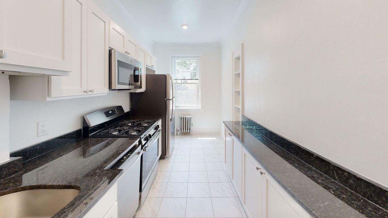 Bright galley kitchen with white cabinetry, black granite countertops, and stainless steel appliances.