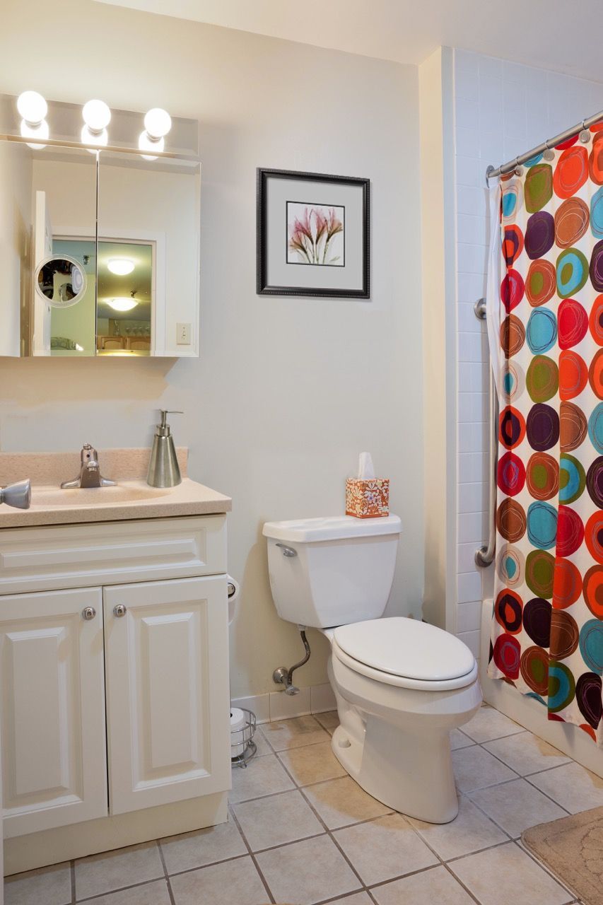 Bathroom in an apartment with vanity, mirror, toilet, and colorful shower curtain.