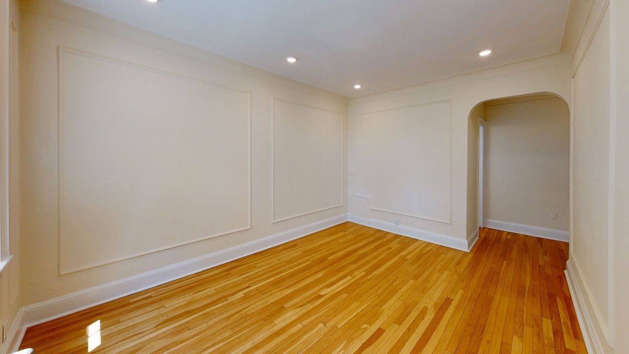 Empty apartment living room with light beige walls, recessed lights, and hardwood flooring.