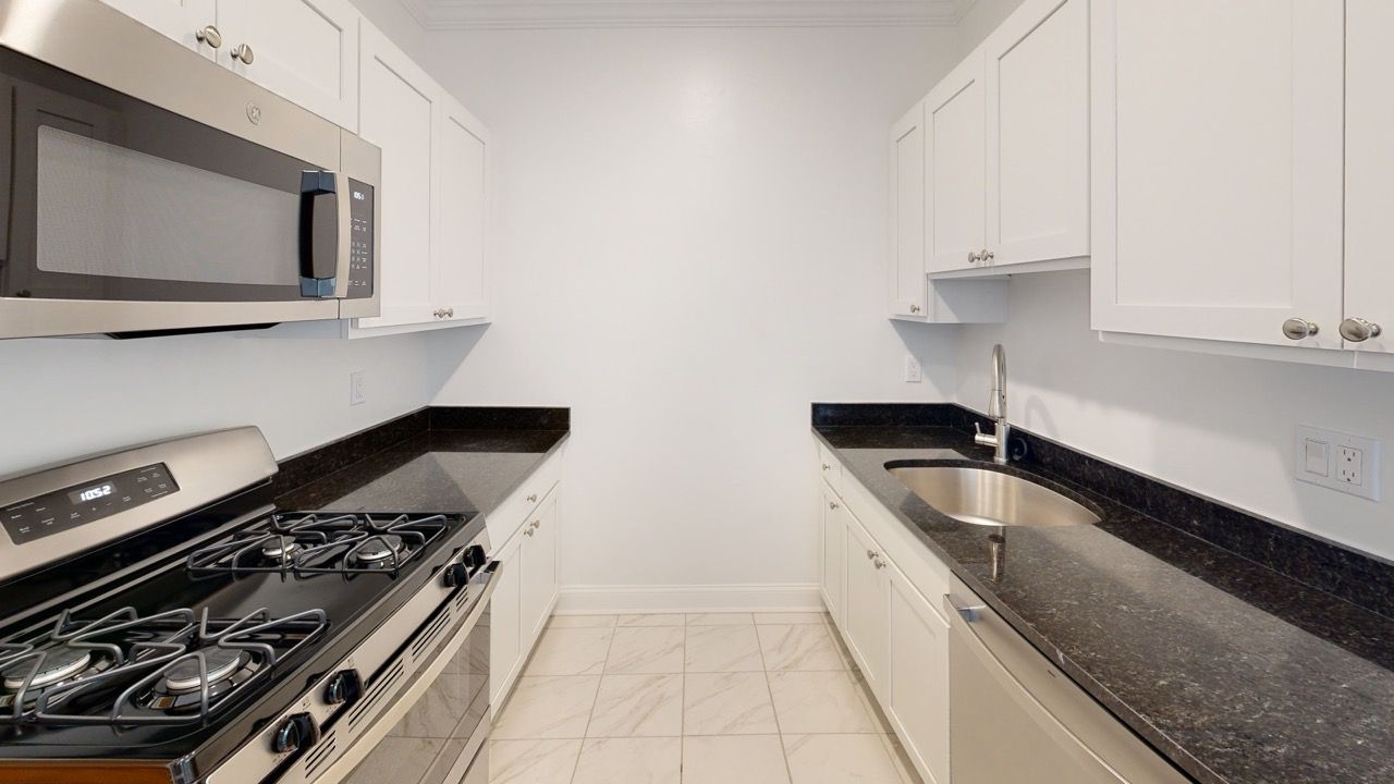 Galley-style kitchen with white cabinetry, black granite countertops, and stainless steel appliances.