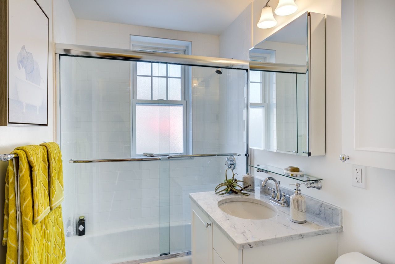 Bathroom with marble countertop, glass shower enclosure, and a yellow towel.