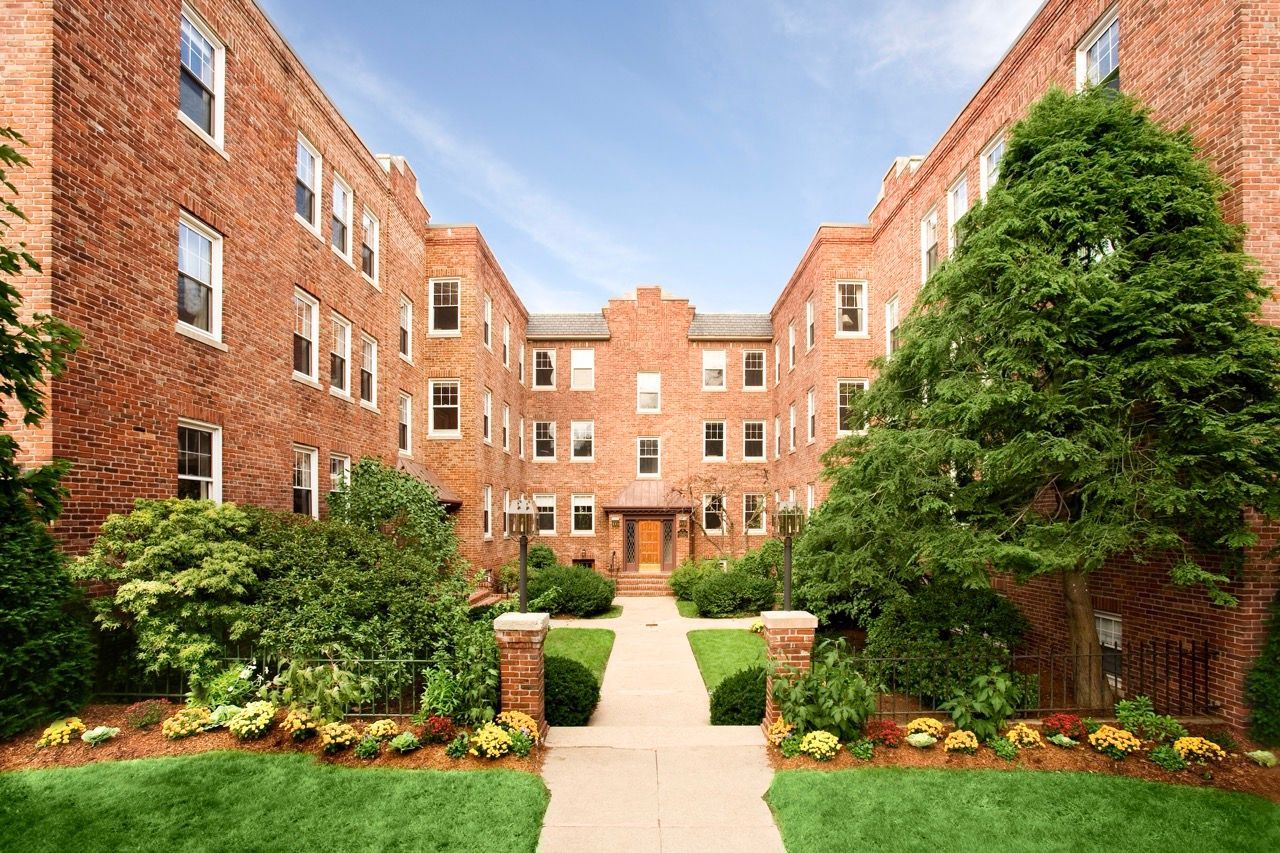 Brick apartment building courtyard with a central path, flanked by shrubs and flowering beds.