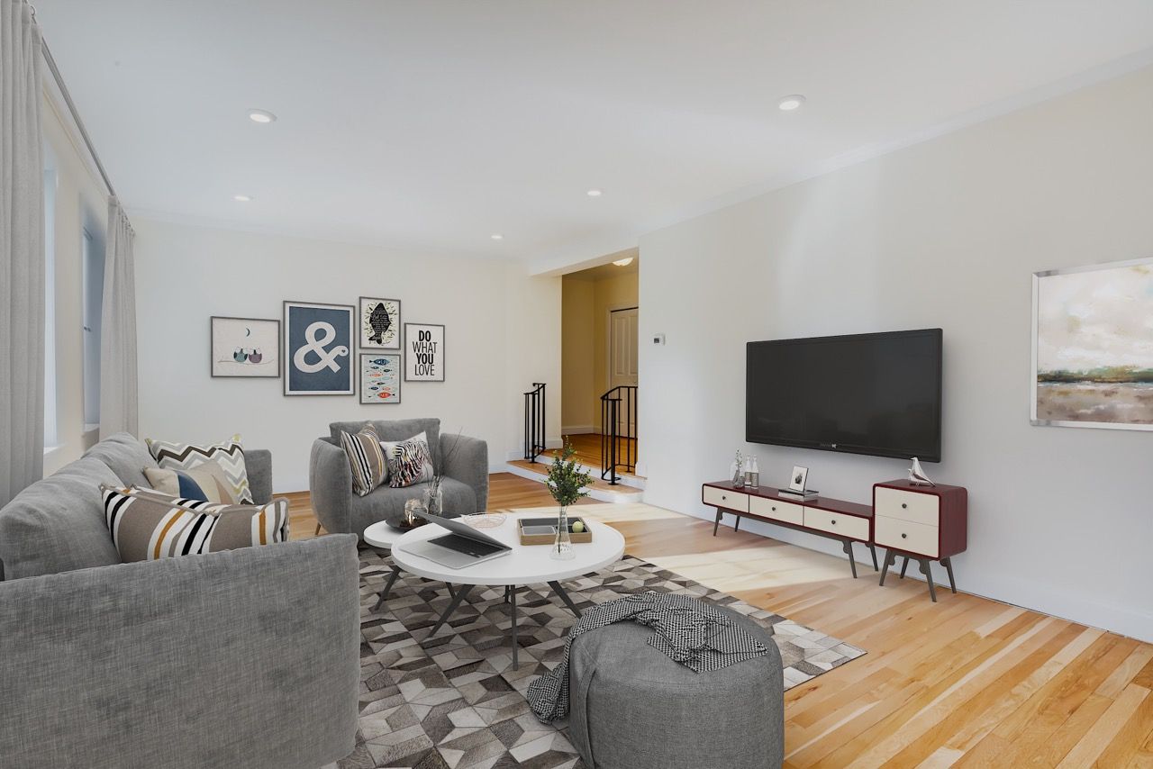 Modern apartment living room with gray sofa, round white coffee table, TV, and light hardwood floors.