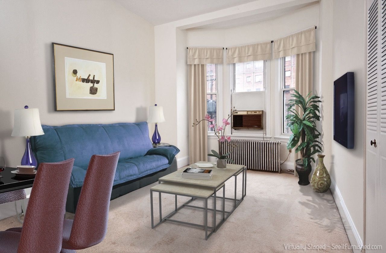 Furnished living room in an apartment with a blue sofa, two nested coffee tables, plants, and a window AC unit.