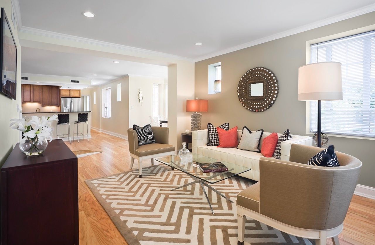 Open-concept living room with beige sofa, two chairs, glass coffee table, and a geometric rug.