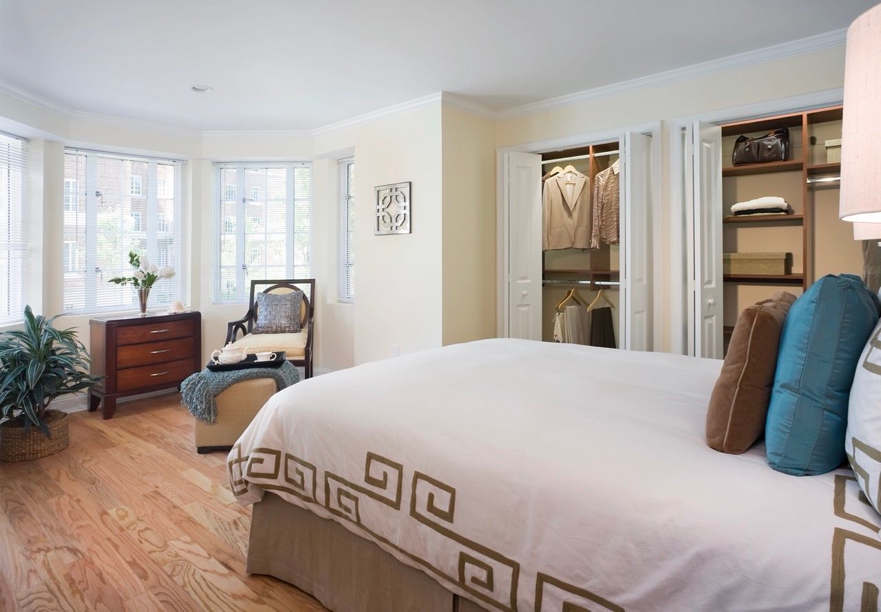 Bright bedroom with a large window, bed, dresser, chair, and open closet.