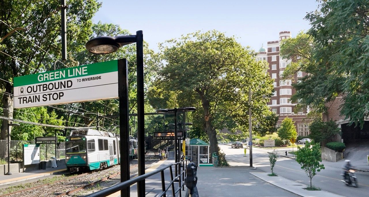 Outdoor train stop with Green Line sign, rails, and trees.